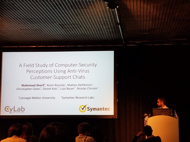 A student standing at a podium next to a powerpoint slide with the title "A Field Study of Computer-Security Perceptions Using Anti-Virus Customer-Support Chats."