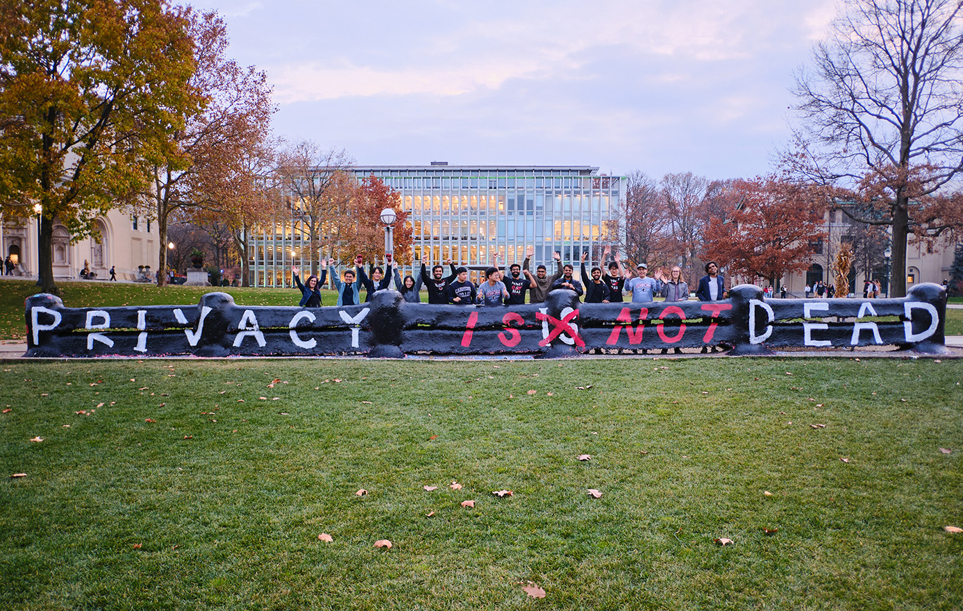 photo of Privacy Engineering students standing in front of a painted fence on the CMU campus  with the painted text "Privacy is Not Dead"
