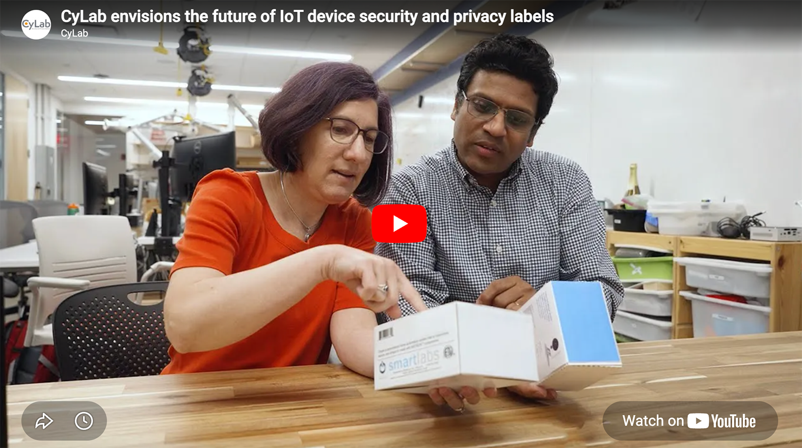Two researchers in a lab examine and point to details on a smart device product box.